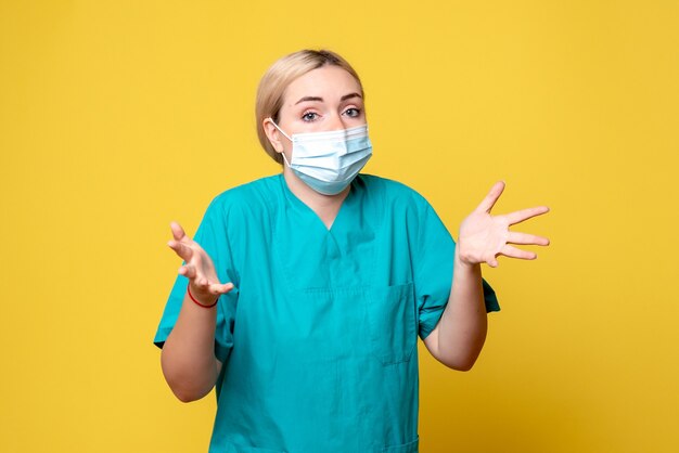 Vue de face de la jeune femme médecin en chemise médicale et masque sur mur jaune