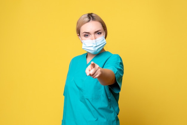 Vue de face de la jeune femme médecin en chemise médicale et masque sur mur jaune