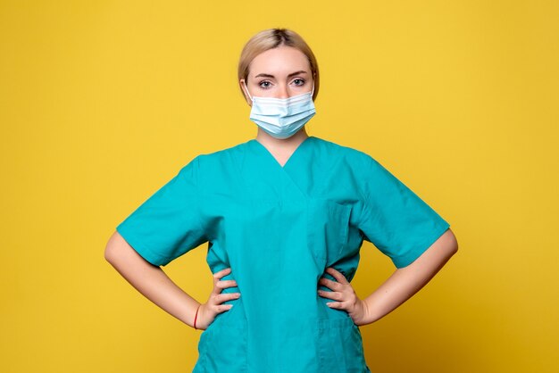 Vue de face de la jeune femme médecin en chemise médicale et masque sur mur jaune