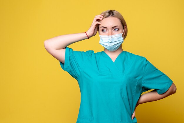 Vue de face de la jeune femme médecin en chemise médicale et masque sur mur jaune