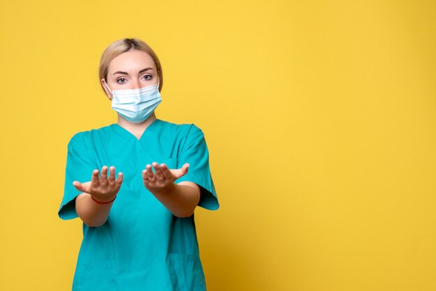 Vue de face de la jeune femme médecin en chemise médicale et masque sur mur jaune