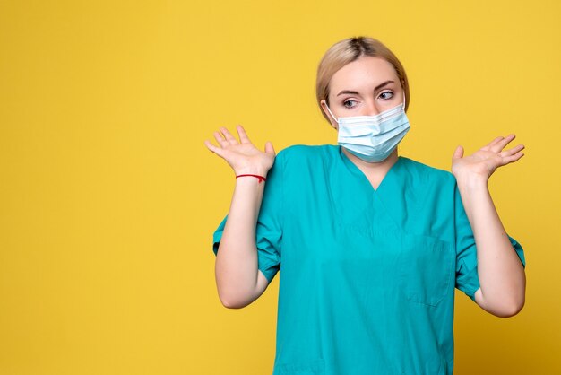 Vue de face de la jeune femme médecin en chemise médicale et masque sur mur jaune