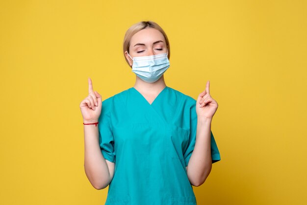 Vue de face de la jeune femme médecin en chemise médicale et masque sur mur jaune