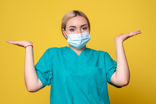 Vue de face de la jeune femme médecin en chemise médicale et masque stérile sur mur jaune