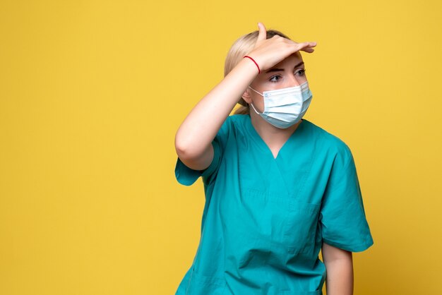 Vue de face de la jeune femme médecin en chemise médicale et masque stérile sur mur jaune