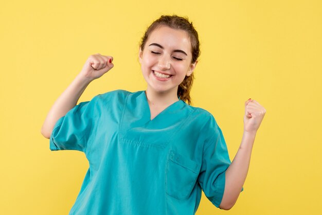 Vue de face de la jeune femme médecin en chemise médicale sur mur jaune