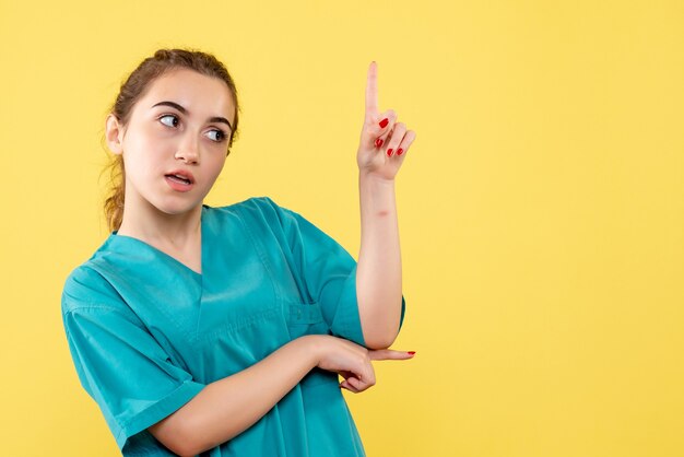 Vue de face de la jeune femme médecin en chemise médicale sur mur jaune