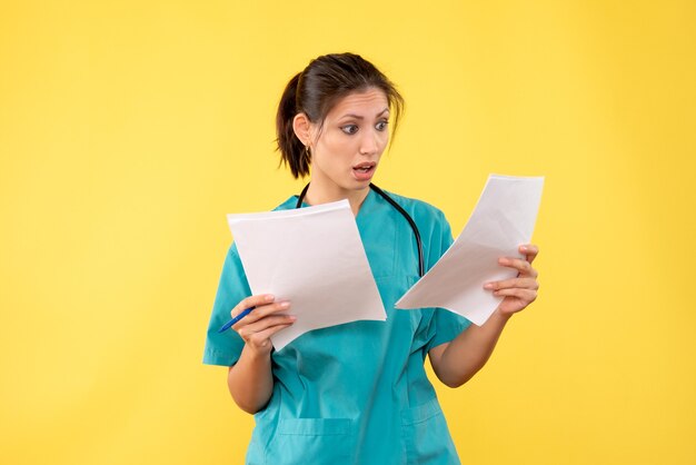 Vue de face jeune femme médecin en chemise médicale avec des papiers sur fond jaune