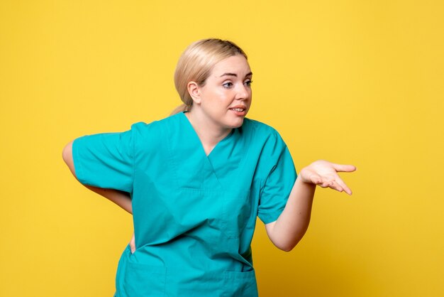 Vue de face de la jeune femme médecin en chemise médicale parler à quelqu'un sur le mur jaune