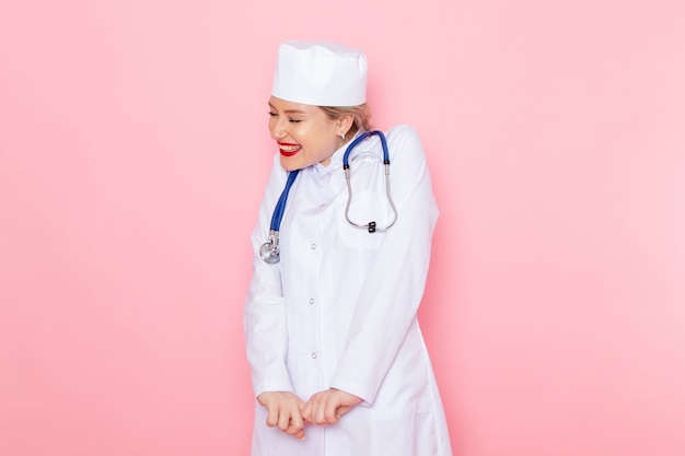 Vue de face jeune femme médecin en costume blanc avec stéthoscope bleu souriant et posant sur le médecin de l'hôpital médical médecine de travail de l'espace rose