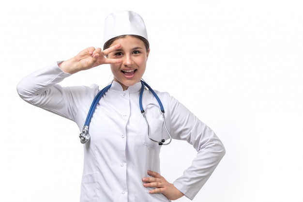 Une vue de face jeune femme médecin en costume médical blanc avec stéthoscope bleu souriant et posant