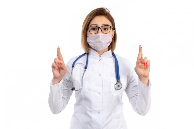 Une vue de face jeune femme médecin en costume médical blanc avec stéthoscope portant un masque de protection blanc sur le blanc