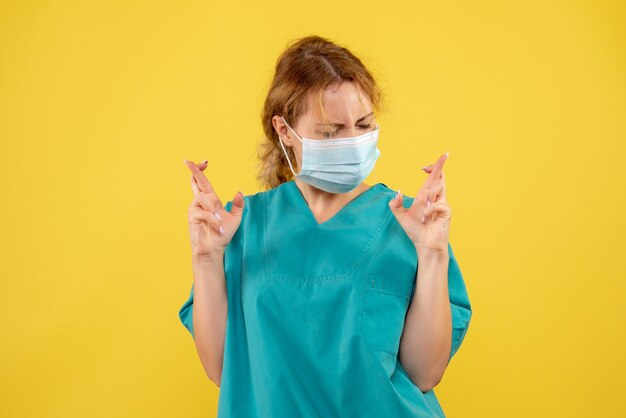 Vue de face de la jeune femme médecin en costume médical et masque sur mur jaune