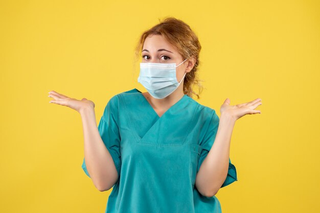 Vue de face de la jeune femme médecin en costume médical et masque sur mur jaune