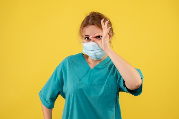 Vue de face de la jeune femme médecin en costume médical et masque sur mur jaune