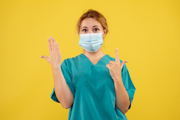 Vue de face de la jeune femme médecin en costume médical et masque sur mur jaune