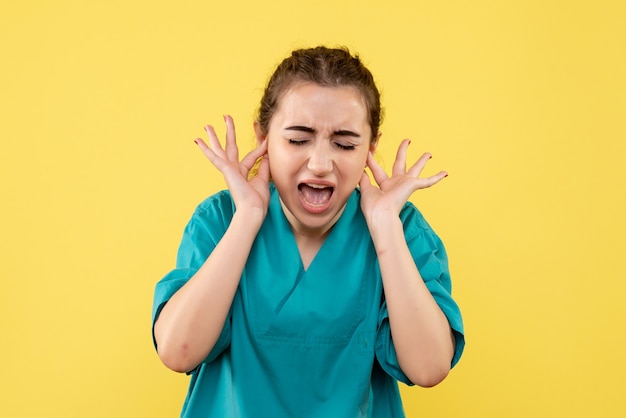 Vue de face jeune femme médecin en costume médical avec les oreilles fermées sur fond jaune