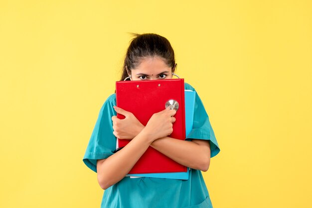 Vue de face de la jeune femme médecin couvrant son visage avec des documents sur le mur jaune