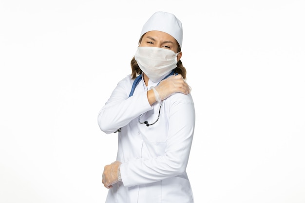 Vue de face jeune femme médecin avec masque stérile et gants en raison d'un coronavirus sur un bureau blanc clair