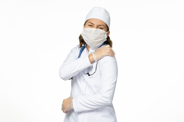 Vue de face jeune femme médecin avec masque stérile et gants en raison d'un coronavirus sur un bureau blanc clair