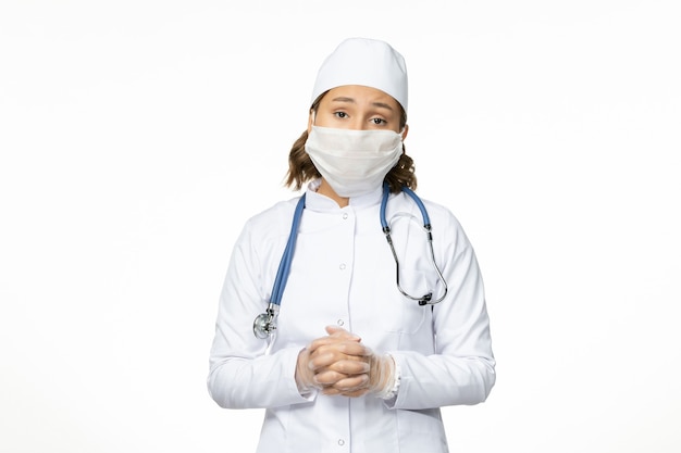 Vue de face jeune femme médecin avec masque stérile et gants en raison d'un coronavirus sur un bureau blanc