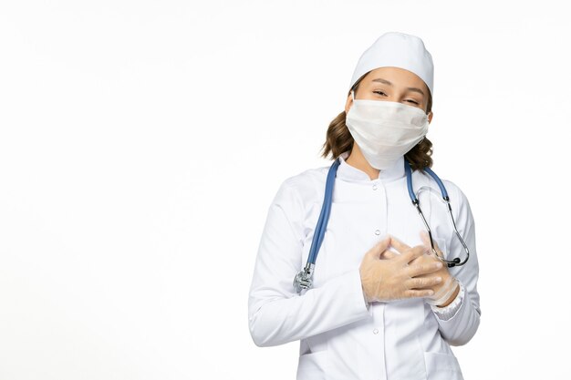 Vue de face jeune femme médecin avec masque stérile et gants en raison d'un coronavirus sur la surface blanche claire