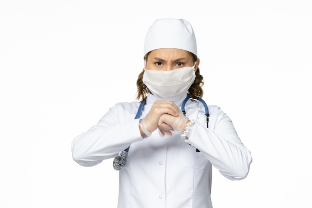 Vue de face jeune femme médecin avec masque stérile et gants en raison d'un coronavirus sur une surface blanche