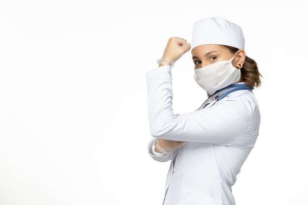 Vue de face jeune femme médecin avec masque stérile et gants en raison du coronavirus le combattant sur une surface blanche