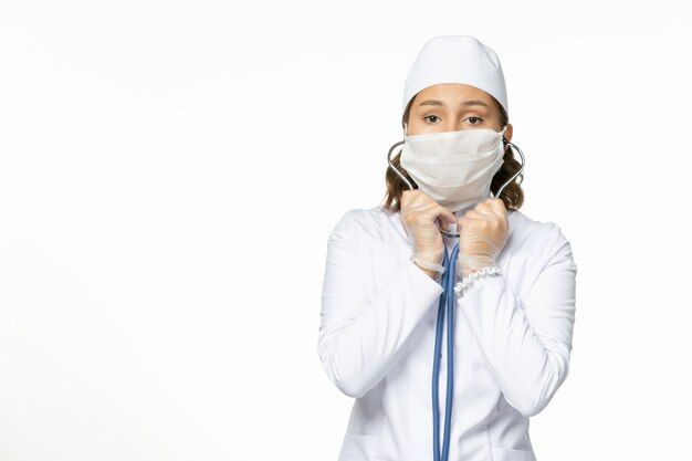 Vue de face jeune femme médecin avec masque stérile en raison d'un coronavirus sur un bureau blanc