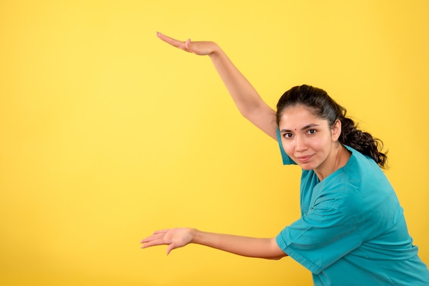 Vue De Face De La Jeune Femme Médecin Montrant La Taille Avec Les Mains Sur Le Mur Jaune