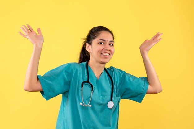 Vue de face de la jeune femme médecin ouvrant les mains sur le mur jaune