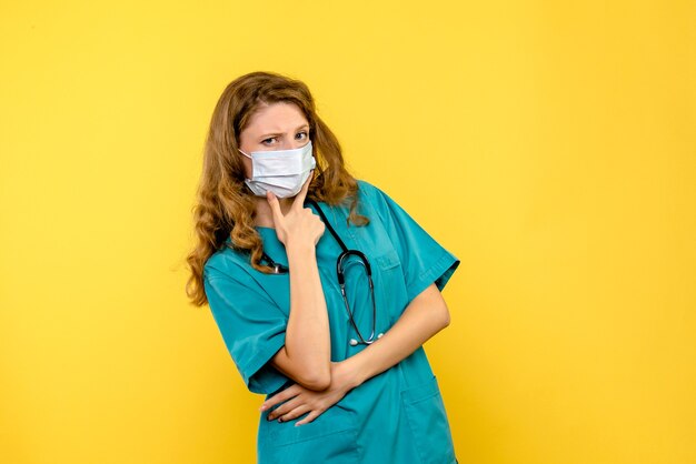 Vue de face jeune femme médecin pensant au masque sur l'espace jaune