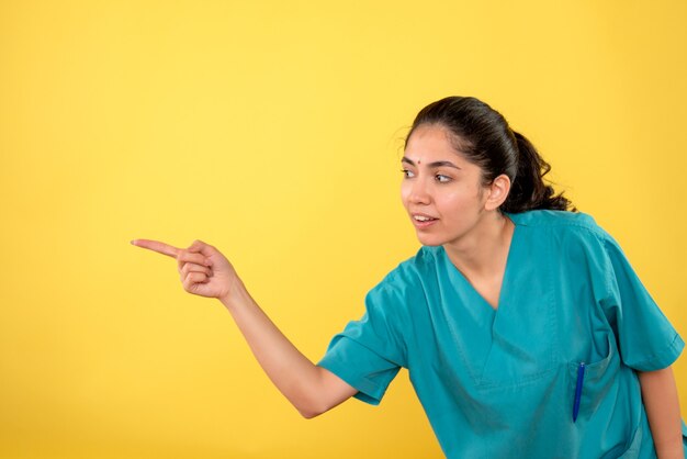 Vue de face de la jeune femme médecin pointant avec le doigt à gauche sur le mur jaune