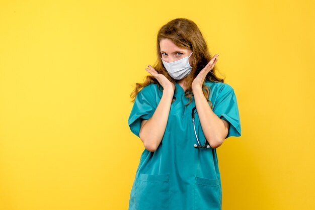 Vue de face jeune femme médecin posant en masque sur l'espace jaune