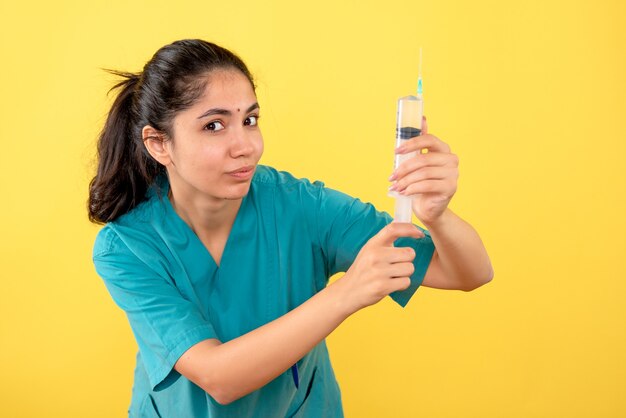 Vue de face de la jeune femme médecin avec une seringue debout sur un mur jaune