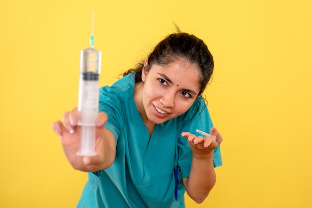 Vue de face de la jeune femme médecin avec seringue sur mur jaune