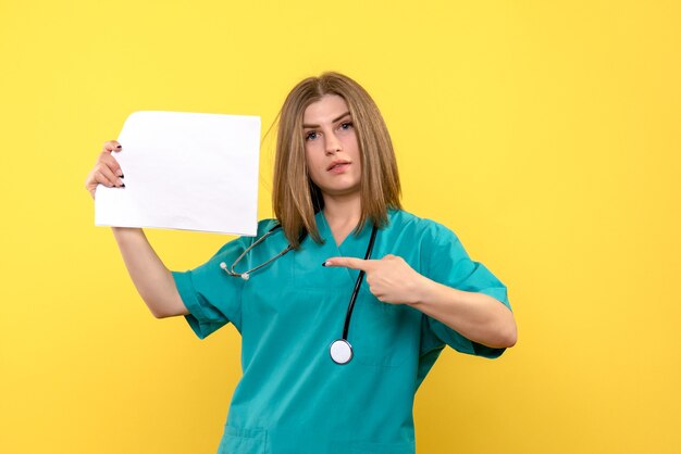 Vue de face de la jeune femme médecin tenant des fichiers sur mur jaune