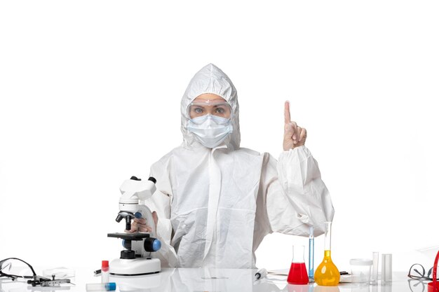 Vue de face jeune femme médecin en tenue de protection blanche avec masque en raison de covid travaillant sur fond blanc virus pandémique splash santé covid