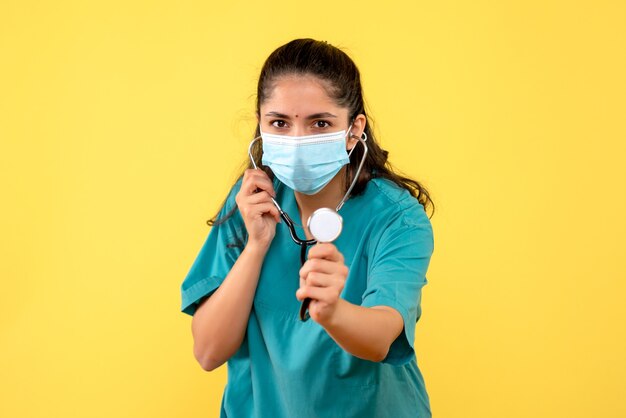 Vue de face jeune femme médecin en uniforme tenant stéthoscope debout sur fond jaune