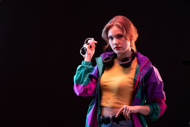 Une vue de face jeune femme moderne en manteau coloré orange t-shirt avec des écouteurs noirs et des lunettes de soleil posant