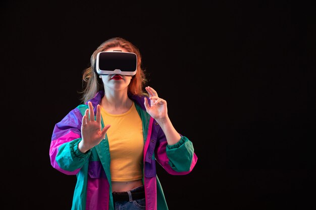 Une vue de face jeune femme moderne en manteau coloré orange t-shirt jouant la réalité virtuelle sur le fond noir jeu interactif