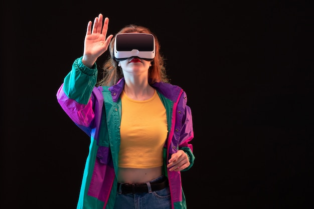 Une vue de face jeune femme moderne en manteau coloré orange t-shirt jouant la réalité virtuelle sur le fond noir jeu interactif