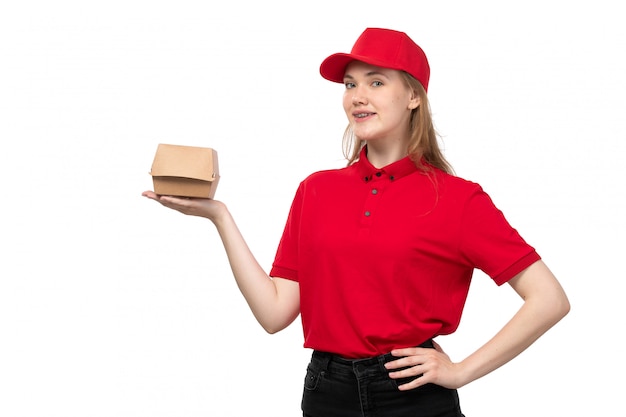 Une vue de face jeune femme ouvrière de messagerie de service de livraison de nourriture souriant tenant le paquet de livraison de nourriture sur blanc