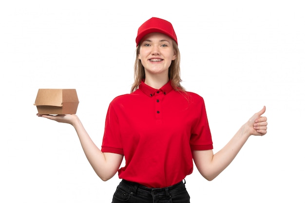 Une vue de face jeune femme ouvrière de messagerie de service de livraison de nourriture souriant tenant le paquet de livraison de nourriture sur blanc