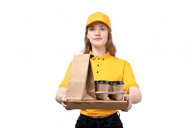 Une vue de face jeune femme ouvrière de messagerie de service de livraison de nourriture souriant tenant des paquets de nourriture et des tasses à café sur blanc