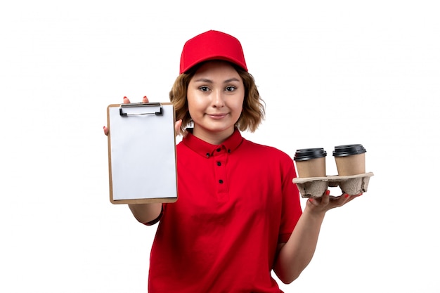 Photo gratuite une vue de face jeune femme ouvrière de messagerie de service de livraison de nourriture tenant le bloc-notes et tasses à café sur blanc