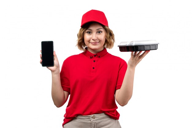 Une vue de face jeune femme ouvrière de messagerie de service de livraison de nourriture tenant un bol avec de la nourriture et un smartphone sur blanc
