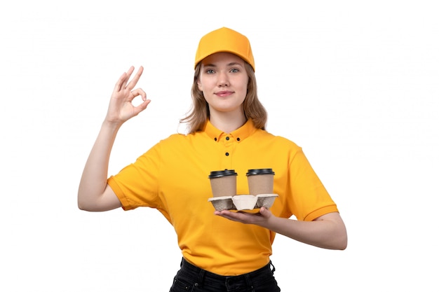 Une vue de face jeune femme ouvrière de messagerie de service de livraison de nourriture tenant des tasses de café souriant sur blanc