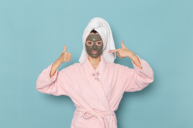 Vue de face jeune femme en peignoir rose après la douche sur le bureau bleu douche crème de bain d'eau de beauté