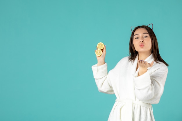vue de face jeune femme en peignoir tenant des tranches de citron sur fond bleu
